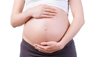 Waiting for a baby. Cropped image of pregnant woman holding hands on her abdomen while standing isolated on white photo