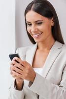 Great news. Beautiful young businesswoman in suit holding mobile and looking at it with smile photo