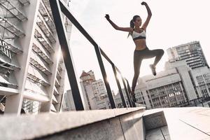 Never stop Full length of modern young woman in sports clothing jumping while exercising outdoors photo