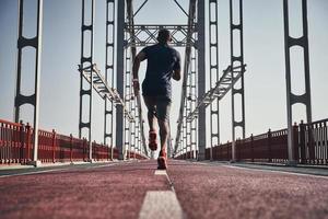 no rendirse nunca. vista trasera completa de un joven africano vestido con ropa deportiva haciendo ejercicio mientras trotaba en el puente al aire libre foto