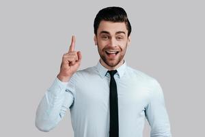 gran idea, un joven apuesto y sonriente con camisa blanca y corbata, con el dedo levantado y mirando a la cámara mientras se enfrenta a un fondo gris foto