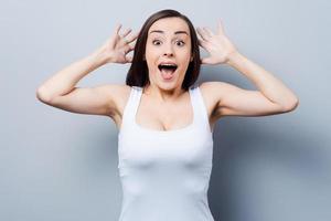 Shocked and happy. Surprised young woman staring at camera while standing against grey background photo