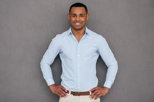 Confident and handsome. Confident young African man keeping arms crossed and looking at camera while standing against grey background photo