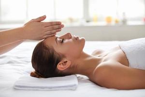 No stress. Beautiful young woman lying on back while massage therapist touching her forehead with hands photo