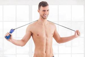 Man with jumping rope. Young muscular man holding a skipping rope on his shoulders and smiling at camera photo