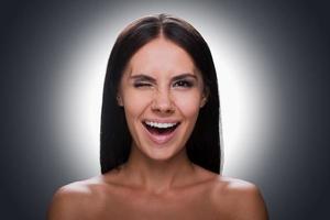 Playful mood. Portrait of beautiful young shirtless woman looking at camera and grimacing while standing against grey background photo