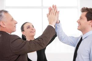 Together we are strong. Three cheerful business people keeping their hands clasped and smiling while standing close to each other photo