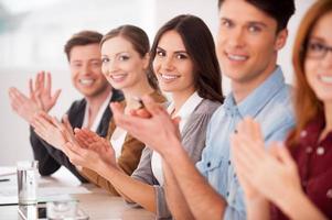 Applauding to you. Group of young people sitting together at the table and applauding to you photo