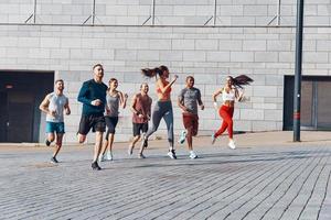 toda la longitud de los jóvenes en ropa deportiva trotando mientras hacen ejercicio al aire libre foto