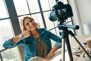 Beautiful young woman gesturing and smiling while working in front of digital camera photo