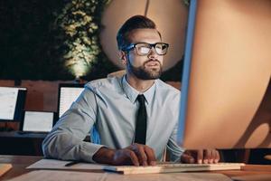 Confident young man working on computer while staying late in the office photo