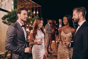 Group of people in formalwear communicating and smiling while spending time on luxury party photo