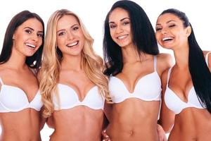 en forma y hermosa. cuatro hermosas mujeres alegres en lencería uniéndose entre sí y sonriendo mientras están de pie contra el fondo blanco foto