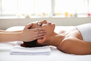 Letting the stress away. Beautiful young woman lying on back while massage therapist touching her face photo