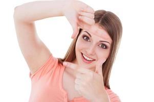 Focus on me Beautiful young smiling woman looking at camera and gesturing finger frame while standing isolated on white photo