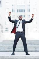 The best day ever Full length of happy young African man in formalwear keeping arms raised and expressing positivity while standing outdoors photo