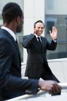 Hi there Cheerful mature man in formalwear moving up by stairs and waving to his colleague photo