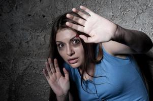 Please no Terrified young woman looking at camera and stretching out hand while leaning at the dark wall photo