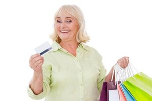 I love shopping Happy senior woman showing her credit card and holding shopping bags while standing isolated on white background photo