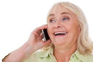 gran noticia feliz anciana hablando por teléfono móvil y sonriendo mientras está de pie aislado sobre fondo blanco. foto