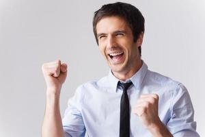 qué gran día feliz joven con camisa y corbata gesticulando y sonriendo mientras está de pie contra el fondo gris foto