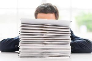 So much work to do Businessman hiding behind a stack of documents laying on the table photo