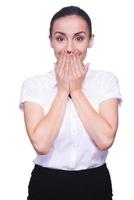 Surprised businesswoman. Surprised young woman in formalwear looking at camera and covering mouth with hands while standing isolated on white photo