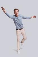 Always winning. Full length of handsome young man looking at camera with smile and gesturing while standing against grey background photo