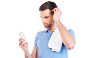 Frustrated father. Frustrated young man with towel on shoulder holding bottle with milk and looking at it while standing against white background photo