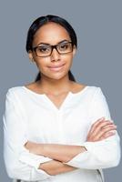 Confident look. Attractive young African woman adjusting her eyeglasses and looking at camera while standing against grey background photo