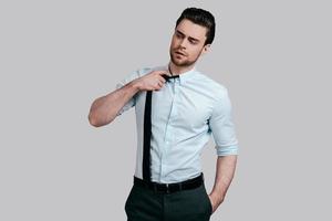 Feeling tired.  Exhausted young man in formalwear looking away and taking off his tie while standing against grey background photo