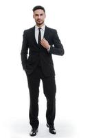 Portrait of elegance. Full length of handsome young man in full suit adjusting his jacket and holding one hand in pocket while standing against white background photo