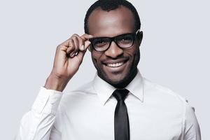 Handsome professional.  Portrait of handsome African man adjusting his eyeglasses and smiling while standing against grey background photo