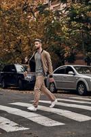 Always careful. Full length of handsome young man in casual wear walking across a zebra crossing while spending time outdoors photo