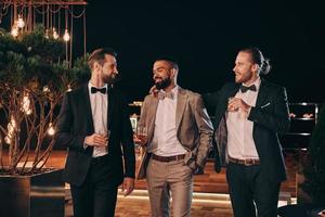 Three handsome men in suits drinking whiskey and communicating while spending time on party photo