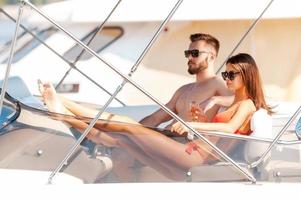 Spending carefree time on yacht. Beautiful young couple looking forward while sitting on the board of yacht photo