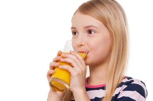 bebiendo jugo de naranja. niña alegre bebiendo jugo de naranja y sonriendo mientras está de pie aislado en blanco foto