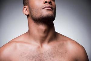 Confidence and masculinity. Cropped image of young shirtless African man standing against grey background photo