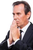 Praying for business success. Side view of thoughtful mature man in formalwear holding hands clasped near face and looking away while standing isolated on white background photo