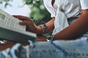 Reading interesting book. Close-up of young woman holding an open book while spending time outdoors photo