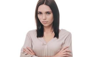 Feeling displeased. Sad young woman in smart casual wear keeping arms crossed and looking at camera while standing against white background photo