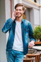 I am already here Cheerful young man talking on the mobile phone and smiling at camera while standing at sidewalk cafe photo