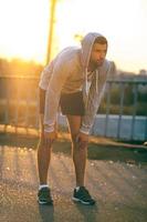 Tired after jogging. Concentrated young man resting after running while standing on the bridge photo