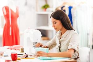 diseñador diligente. vista lateral de una joven cosiendo mientras se sienta en su lugar de trabajo en un taller de moda foto