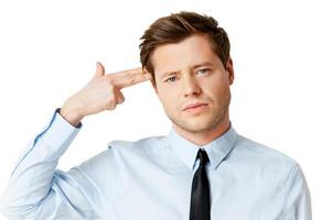 Failed again. Depressed young man in shirt and tie touching his temple with finger gun and looking at camera while standing isolated on white photo