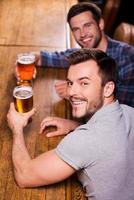 Friends in bar. Top view of two happy young men drinking beer at the bar counter and smiling photo