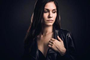 belleza pensativa. bella joven con chaqueta de cuero parada en un fondo gris oscuro foto