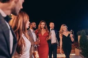 grupo de personas en ropa formal comunicándose y sonriendo mientras pasan tiempo en una fiesta de lujo foto