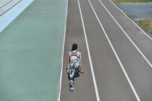 Pushing to the limit. Top rear view of young woman in sports clothing standing on the start line while running outdoors photo