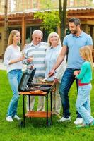 Time for barbeque. Full length of happy family barbecuing meat on grill outdoors photo